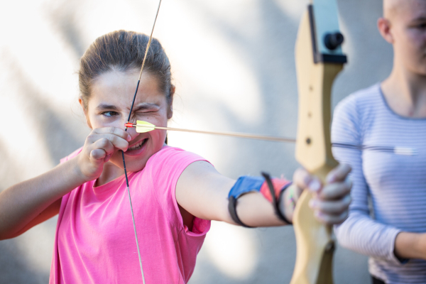 Jeune fille tenant un archer avec une flèche et visant une cible en fermant un oeil.
